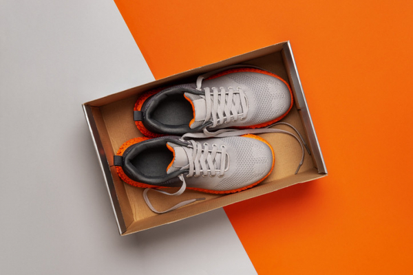photo of a new pair of white and orange sneakers in a box, viewed from above on a white and orange background with an angled division between the colors